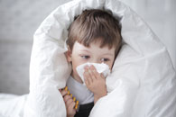 boy in blanket wipes nose