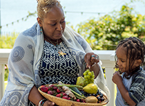 Black elderly woman showig basket of vegetables to young child 